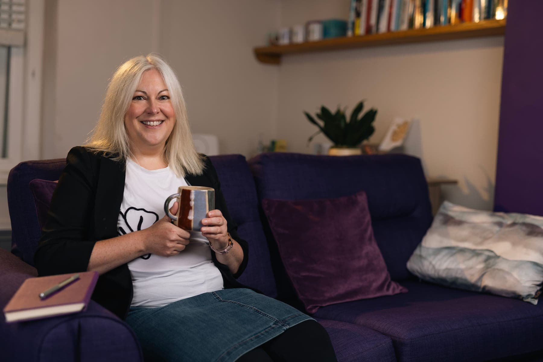Dr Melanie Lee smiling on a sofa with a mug of tea